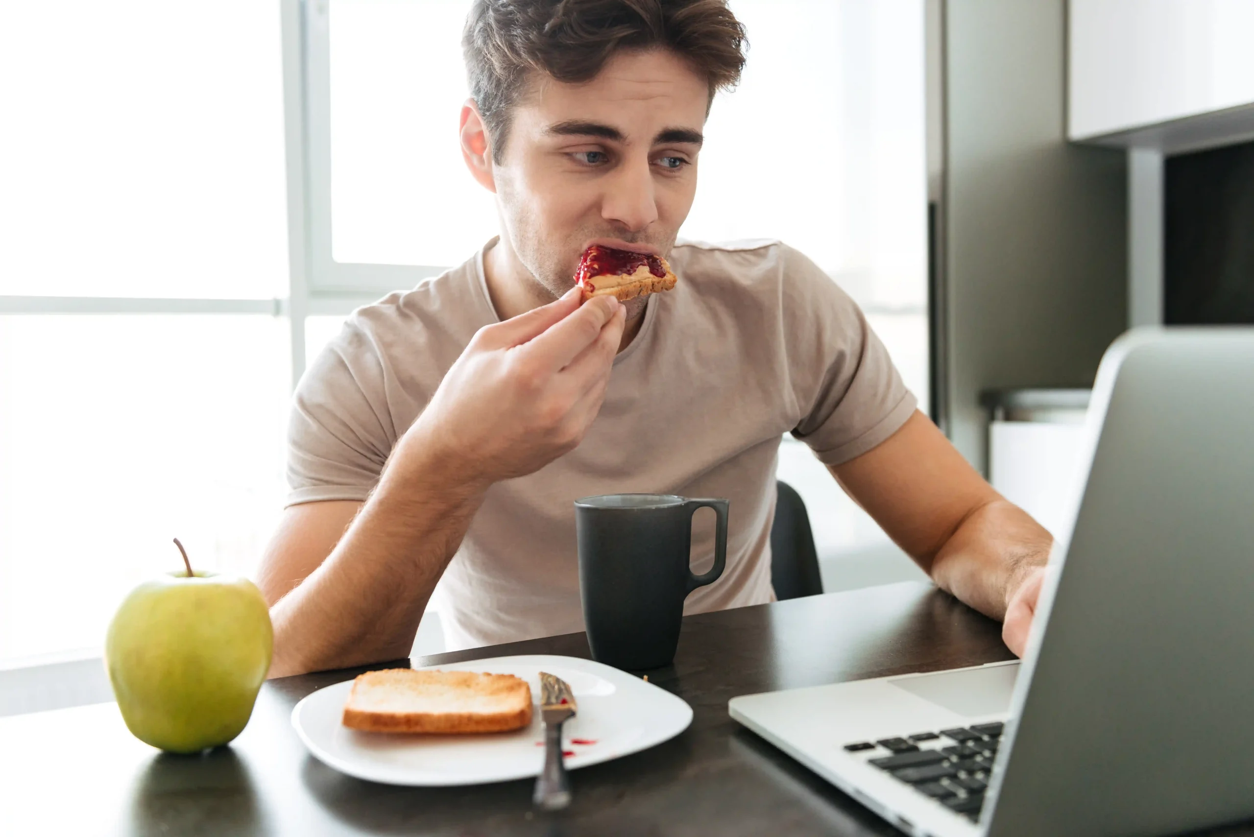 homem-atraente-concentrado-usando-laptop-enquanto-tomando-cafe-da-manha.opti